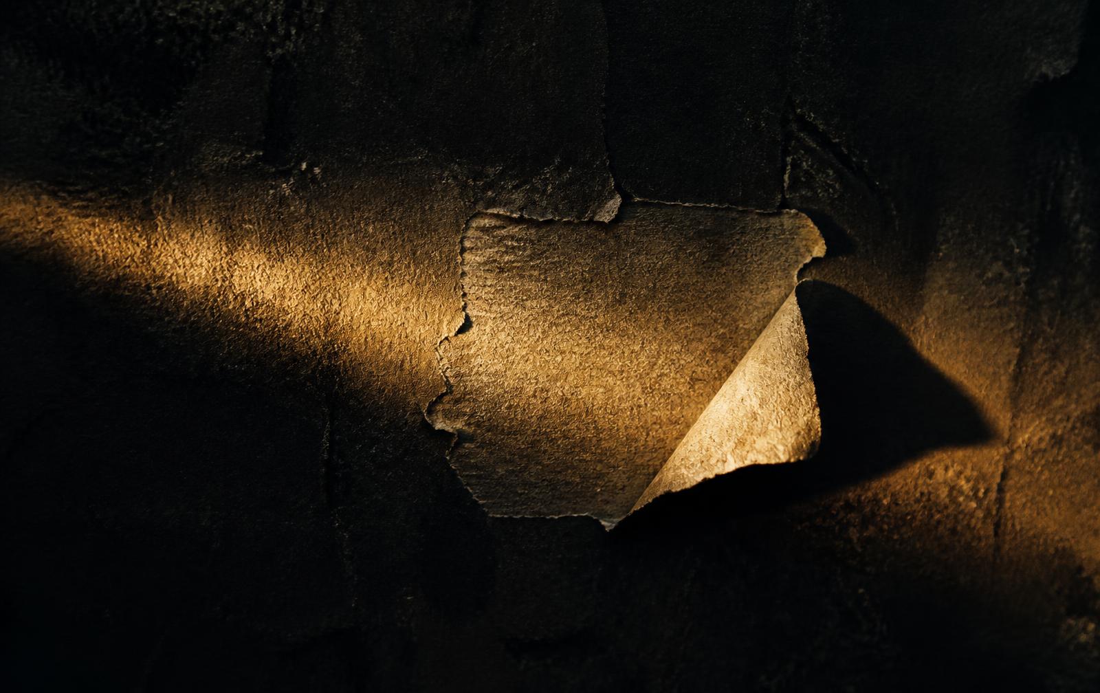 Torn paper label peeling away from a dark surface, lit by warm light